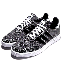 Adidas sneakers with a bright white upper fully covered in bold black spots in true Dalmatian fashion, using irregular organic shapes so the pattern feels natural rather than uniform. The classic three stripes appear in solid black and stand out cleanly against the spotted background. The heel tab uses a vivid red accent as a collar reference, with a small embossed paw print centered above it. The tongue label shows a simple Dalmatian face in black line art. Laces remain bright white, the midsole stays clean off white, and the outsole is deep black to echo the spotting and ground the design visually.